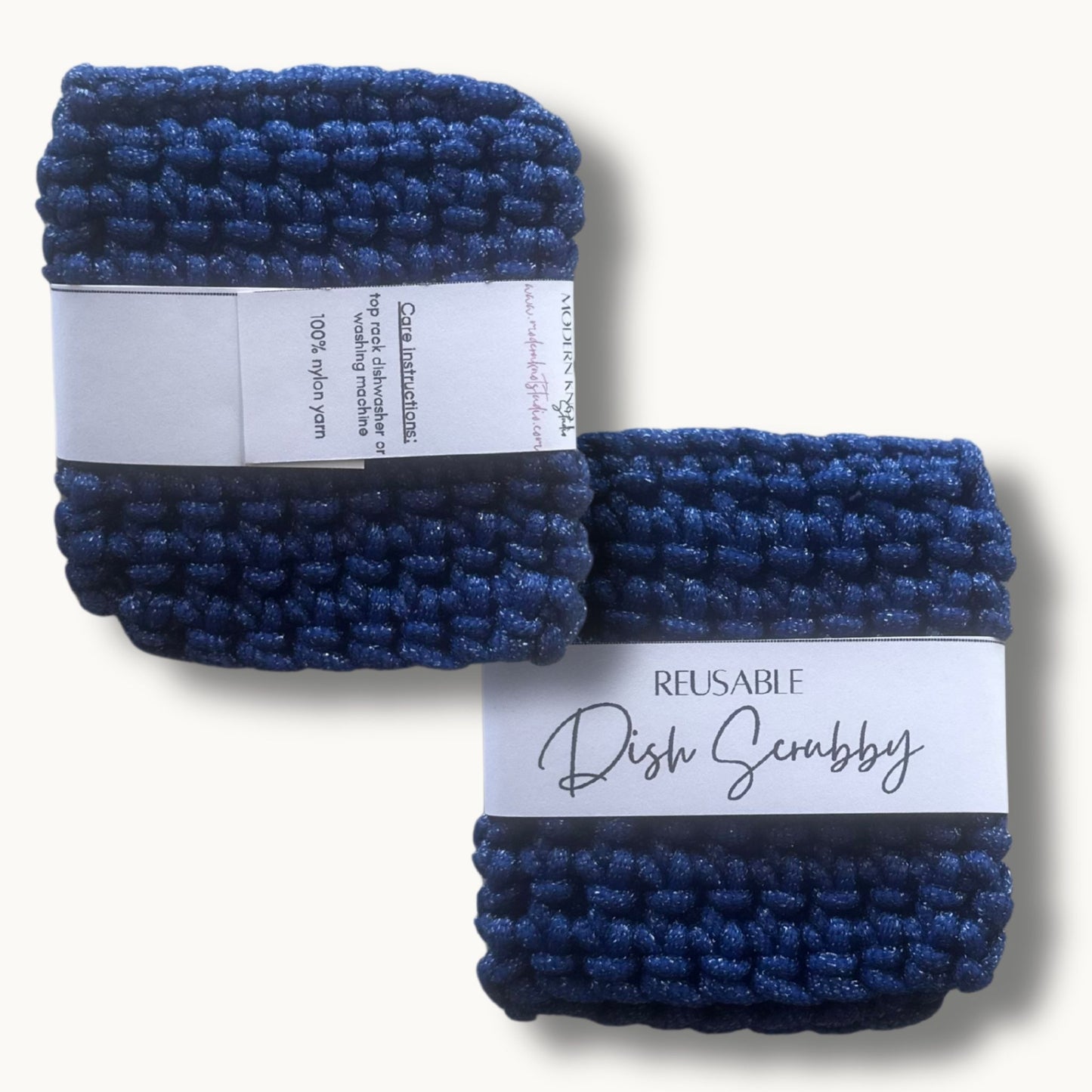 Two blue crochet dish scrubbies with labels, one labeled 'REUSABLE DISH SCRUBBY' and the other with a care instruction label.