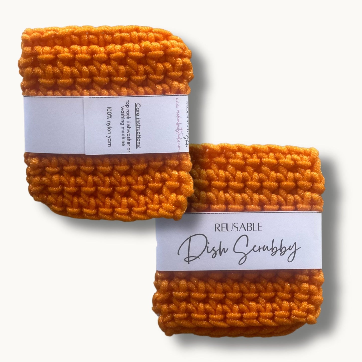 Two orange crochet dish scrubbies with labels, one labeled 'REUSABLE DISH SCRUBBY' and the other with a care instruction label.