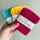 Three colorful reusable dish scrubbers held by a hand against a plain background