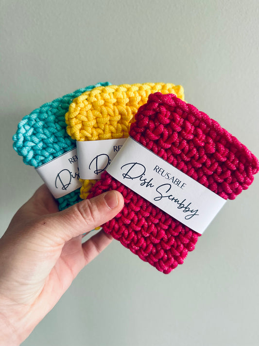 Three colorful reusable dish scrubbers held by a hand against a plain background