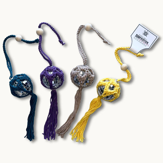 A collection of handmade crochet car charms with a disco ball design, featuring various colors and patterns, attached to a looped tie for hanging in a car's rearview mirror.