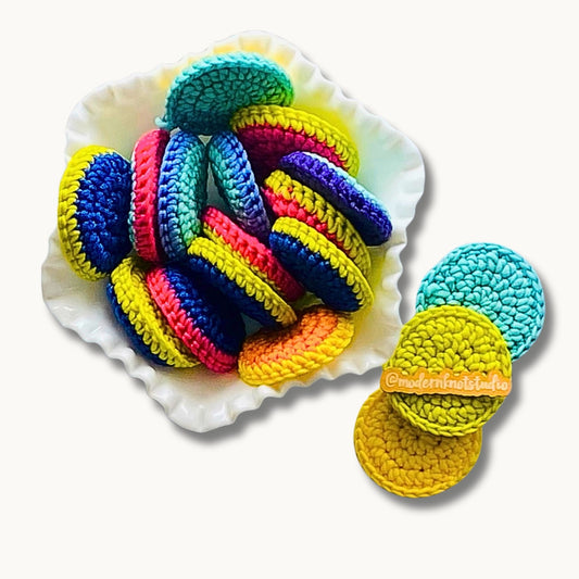 A collection of colorful round dish scrubbies made from yarn in various bright colors, displayed on a white dish.